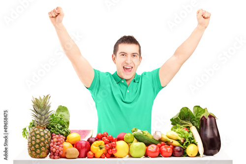 Photo: Excited man raising hands and posing with a pile of fruit and ve Excited man raising hands and posing with a pile of fruit and ve