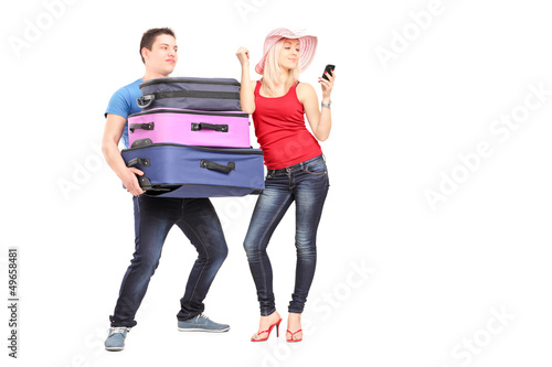 Photo: Frustrated man carrying his girlfriend's baggage while she is ma Frustrated man carrying his girlfriend's baggage while she is ma