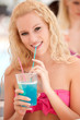 Attractive blonde girl drinks blue cocktail in shadow on a hot s