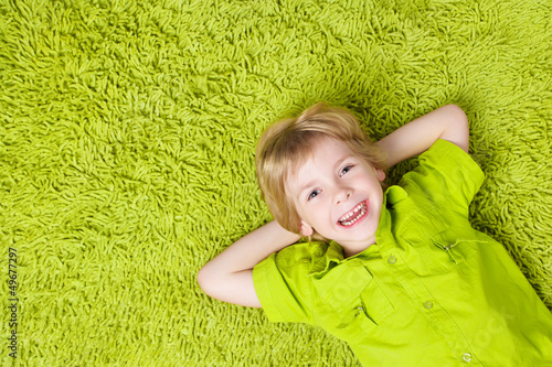 Photo: Happy child lying on the green carpet background. Boy smiling an Happy child lying on the green carpet background. Boy smiling an