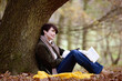 A woman sitting under a tree in autumn time, holding a book