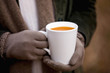A woman holding a cup of soup in autumn time, close up
