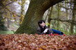 A woman sitting under a tree holding a hot drink in autumn