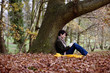 A woman sitting under a tree in autumn time, reading a book