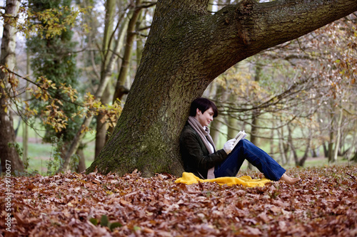 Photo: A woman sitting under a tree in autumn time, reading a book A woman sitting under a tree in autumn time, reading a book