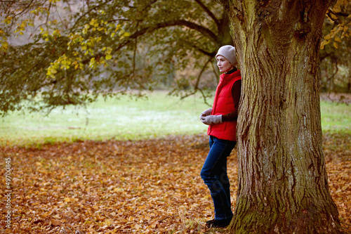 Photo: A woman standing next to a tree in autumn time A woman standing next to a tree in autumn time