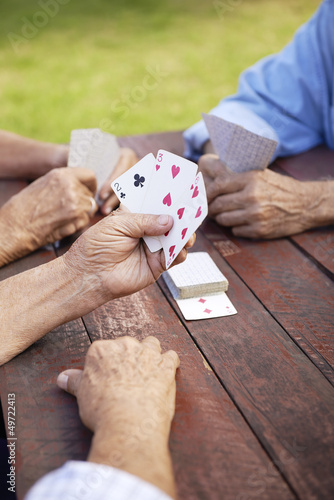 Photo: Active seniors, group of old friends playing cards at park Active seniors, group of old friends playing cards at park