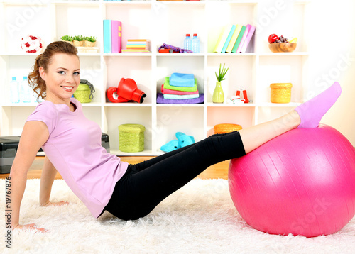 Photo: Young woman doing fitness exercises with gym ball at home Young woman doing fitness exercises with gym ball at home