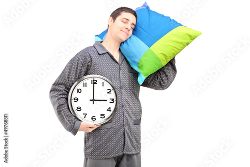 Photo: A young lazy guy holding a wall clock and sleeping on a pillow A young lazy guy holding a wall clock and sleeping on a pillow