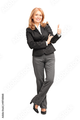 Photo: Full length portrait of a smiling businesswoman leaning on wall Full length portrait of a smiling businesswoman leaning on wall