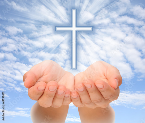Photo: Hands holding Christian cross with light beams over sky Hands holding Christian cross with light beams over sky