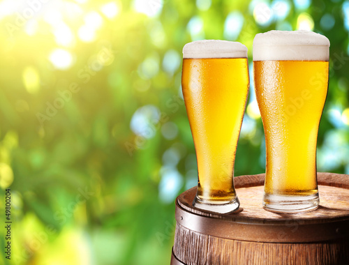 Photo: Two glasses of beer on a wooden barrel. Two glasses of beer on a wooden barrel.