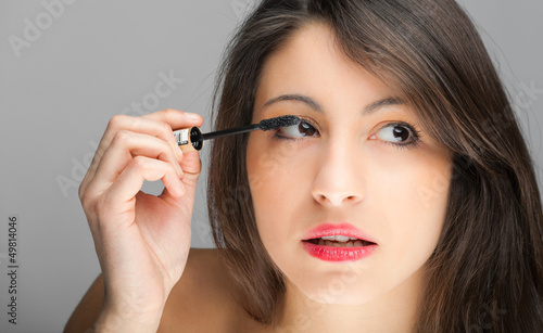 Photo: Pretty young woman applying mascara using lash brush Pretty young woman applying mascara using lash brush
