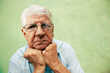 Portrait of serious old man looking at camera with hands on chin