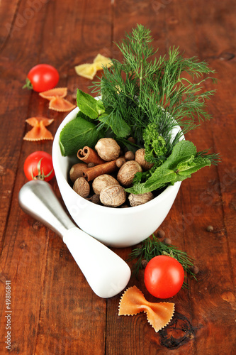 Photo: Herbs and spices in ceramic mortar, on wooden background Herbs and spices in ceramic mortar, on wooden background