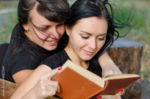 Photo: Two close woman friends enjoying a book Two close woman friends enjoying a book