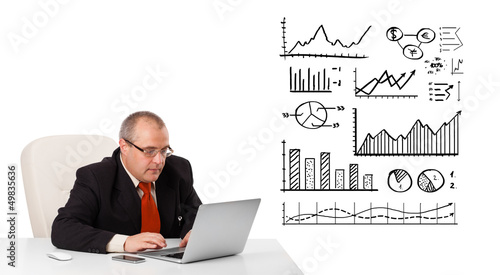Photo: Businessman sitting at desk with diagrams and laptop Businessman sitting at desk with diagrams and laptop