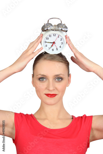 Photo: Smiling woman putting alarm clock on her head Smiling woman putting alarm clock on her head