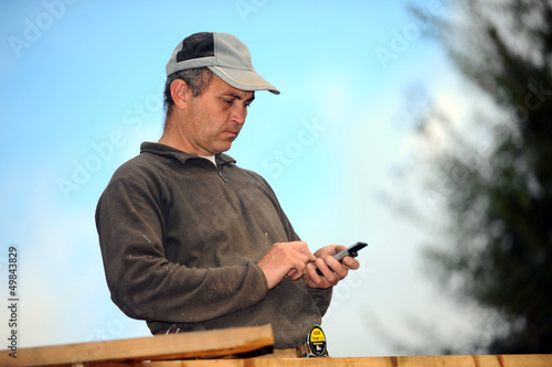 Photo: Carpenter sending text message whilst working outdoors Carpenter sending text message whilst working outdoors