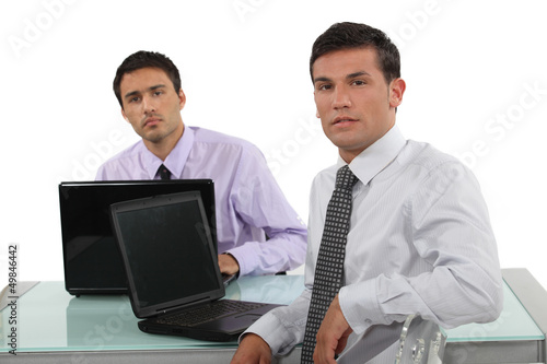 Photo: Two businessmen sat at the same desk Two businessmen sat at the same desk