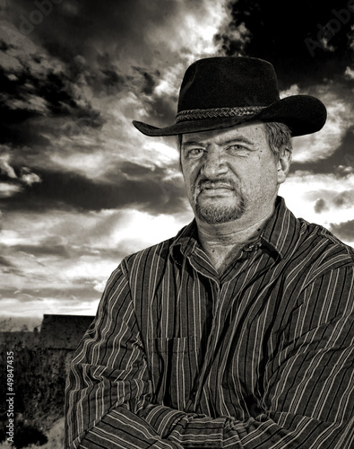 Photo: Rancher scowling with stormy sky in background Rancher scowling with stormy sky in background