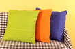 Colorful pillows on couch on yellow background