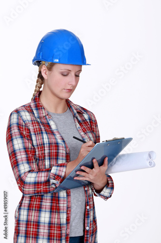 Photo: Female construction worker writing on clip-board Female construction worker writing on clip-board