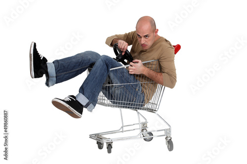 Photo: Man sat in shopping trolley with steering wheel Man sat in shopping trolley with steering wheel