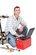Photo: Handyman kneeling by laptop and tool kit Handyman kneeling by laptop and tool kit