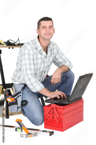 Photo: Handyman kneeling by laptop and tool kit Handyman kneeling by laptop and tool kit