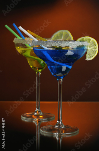 Photo: Yellow and blue cocktails in glasses on color background Yellow and blue cocktails in glasses on color background
