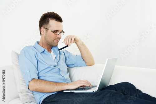 Photo: Man using credit card and laptop on couch Man using credit card and laptop on couch