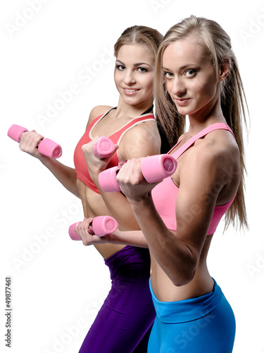 Photo: Two beautiful young woman doing fitness exercise with dumbbells Two beautiful young woman doing fitness exercise with dumbbells