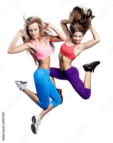 Photo: Two beautiful athletic girl jumping over white background Two beautiful athletic girl jumping over white background