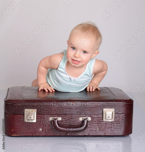 Photo: baby girl playing with suitcase on grey background baby girl playing with suitcase on grey background