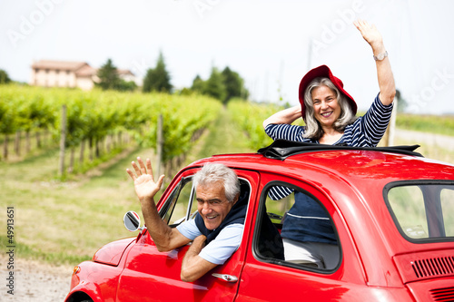 Photo: Mature couple enjoying a road trip in a small red car Mature couple enjoying a road trip in a small red car