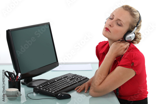 Photo: Blond office worker listening to music at desk Blond office worker listening to music at desk