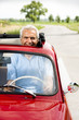 Mature man enjoying a road trip in a small red car