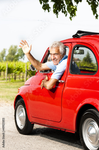 Photo: Mature man enjoying a road trip in a small red car Mature man enjoying a road trip in a small red car
