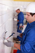 Pair of electricians wiring a white tiled room