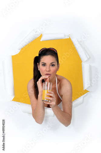 Photo: Woman busting through poster drinking orange juice Woman busting through poster drinking orange juice