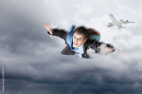 Photo: Young businessman flying with parachute on back Young businessman flying with parachute on back
