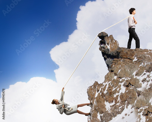 Photo: Two businessmen pulling rope atop of mountain Two businessmen pulling rope atop of mountain