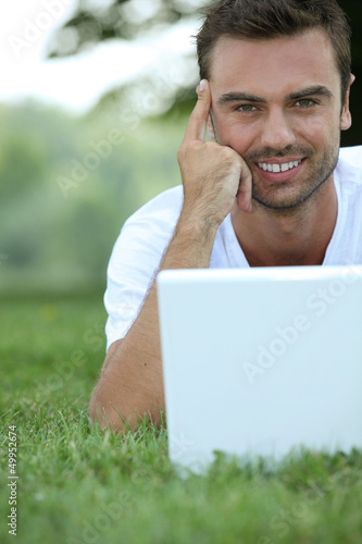 Photo: Man laying in the park surfgin the internet Man laying in the park surfgin the internet