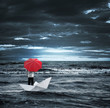 Man with a red umbrella on a paper boat in the stormy sea
