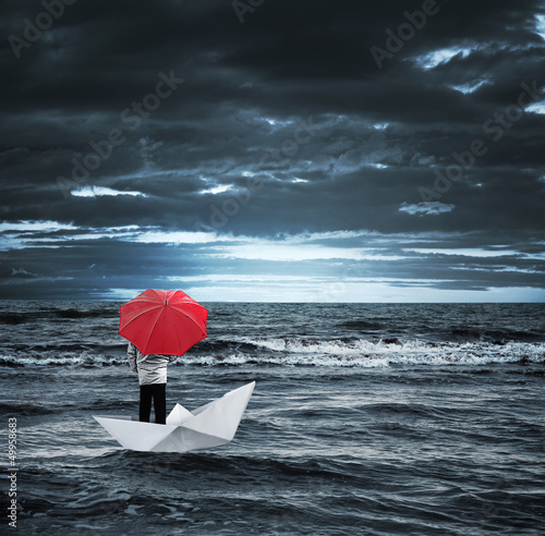 Photo: Man with a red umbrella on a paper boat in the stormy sea Man with a red umbrella on a paper boat in the stormy sea
