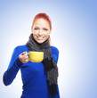 A young and happy woman in a blue sweater holding a cup of tea