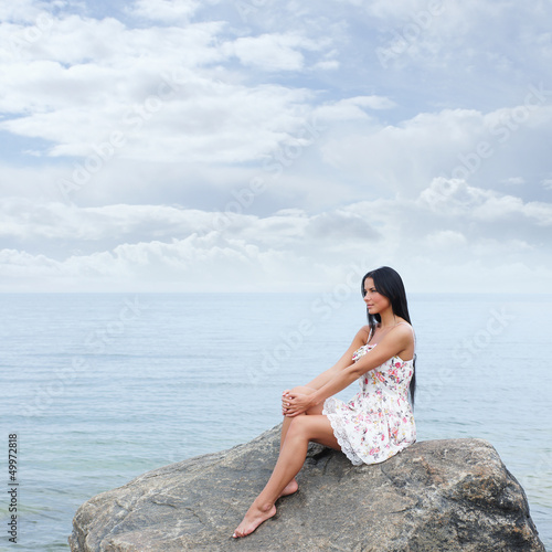 Photo: A young and beautiful brunette woman in a dress near the sea A young and beautiful brunette woman in a dress near the sea
