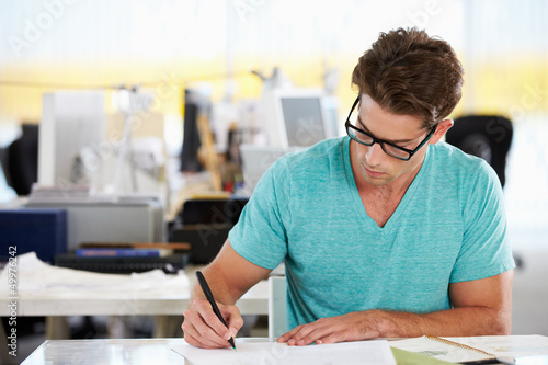 Photo: Man Writing At Desk In Busy Creative Office Man Writing At Desk In Busy Creative Office