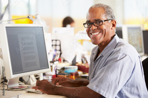Photo: Man Working At Desk In Busy Creative Office Man Working At Desk In Busy Creative Office